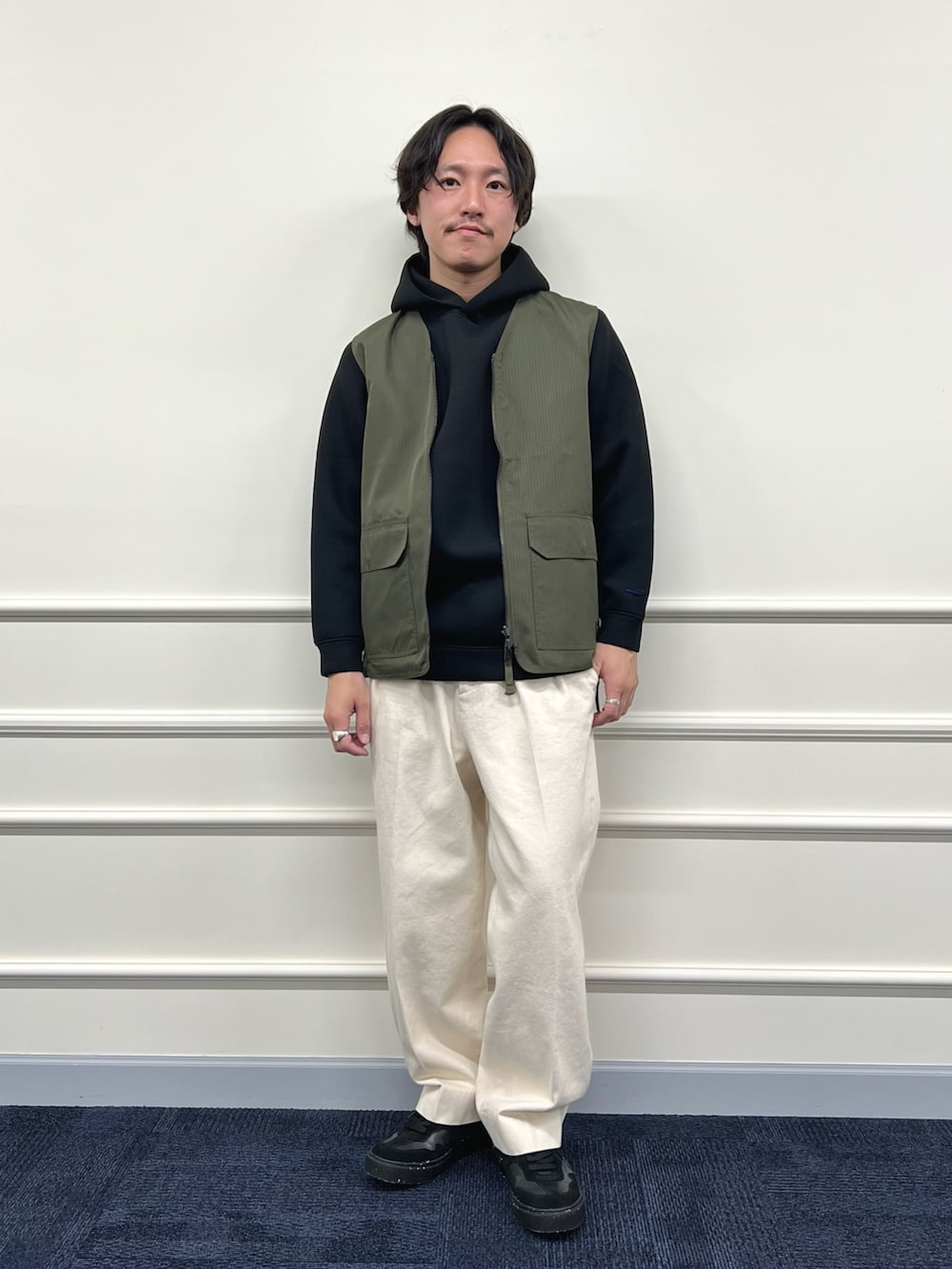 グリーン系のベスト、ブラック系のパーカー、ホワイト系のデニムパンツを着用したメンズの冬コーディネートの2枚目の写真