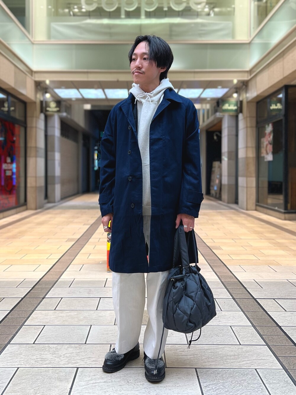 グレー系のパーカー、ブルー系のステンカラーコート、グレー系のトートバッグを着用したメンズの冬コーディネートの2枚目の写真