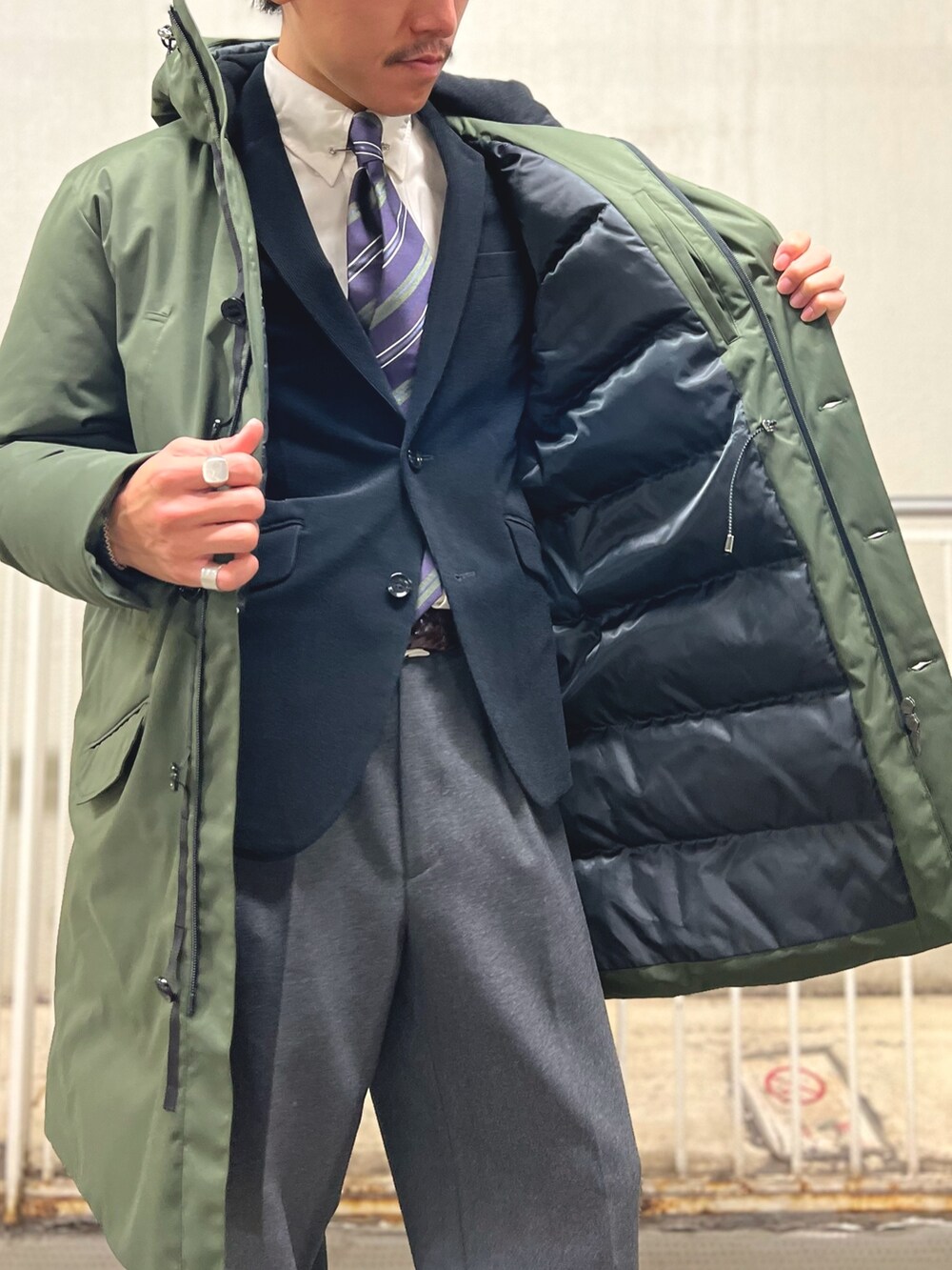 ブルー系のネクタイ、ブラック系のテーラードジャケット、グリーン系のダウンジャケット/コートを着用したメンズの冬コーディネートの7枚目の写真