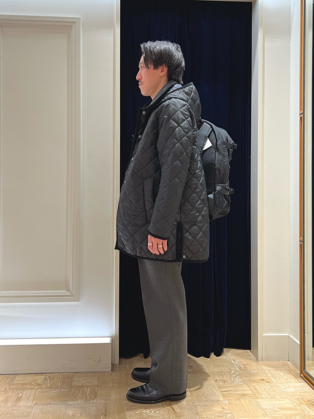 ブラック系のステンカラーコート、ブラック系のローファー、ブラック系のバックパック/リュックを着用したメンズの冬コーディネートの3枚目の写真