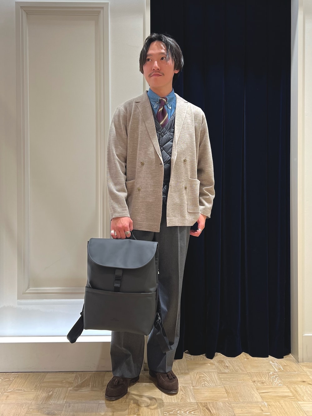 ベージュ系のテーラードジャケット、ブラック系のダウンベスト、ブラック系のバックパック/リュックを着用したメンズの冬コーディネートの6枚目の写真