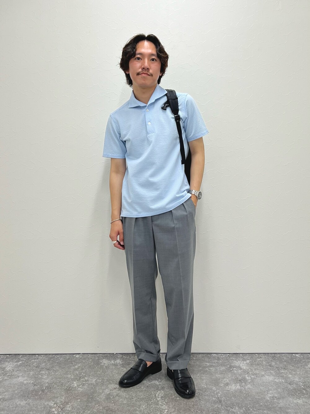 ブルー系のポロシャツ、グレー系のスラックス、ブラック系のバックパック/リュックを着用したメンズの春コーディネートの3枚目の写真