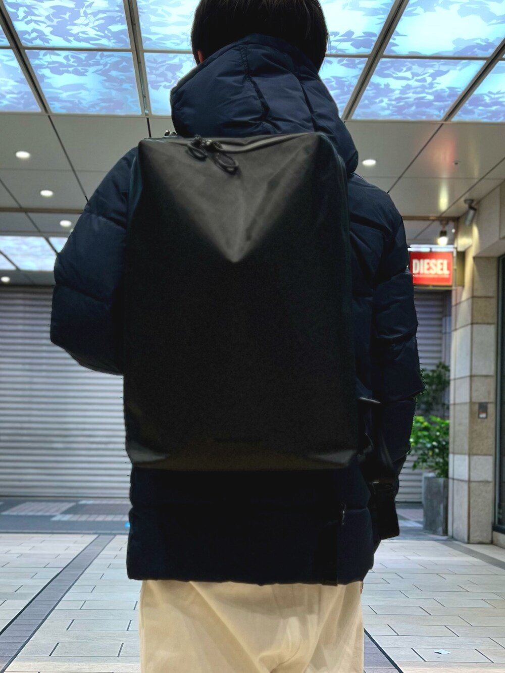 ブラック系のダウンジャケット/コート、ブラック系のバックパック/リュック、ブルー系のシャツ/ブラウスを着用したメンズの春コーディネートの8枚目の写真