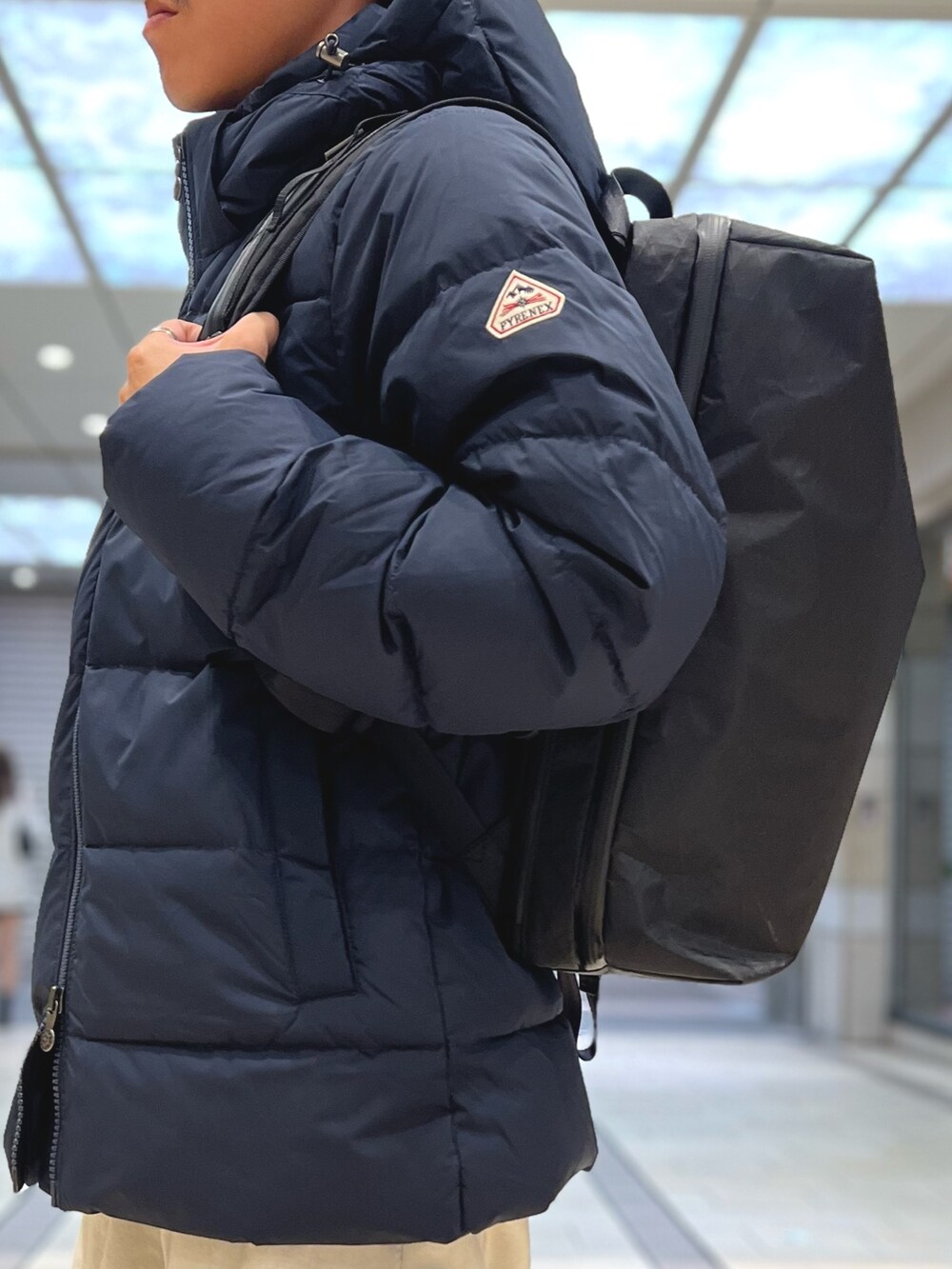 ブラック系のダウンジャケット/コート、ブラック系のバックパック/リュック、ブルー系のシャツ/ブラウスを着用したメンズの春コーディネートの5枚目の写真