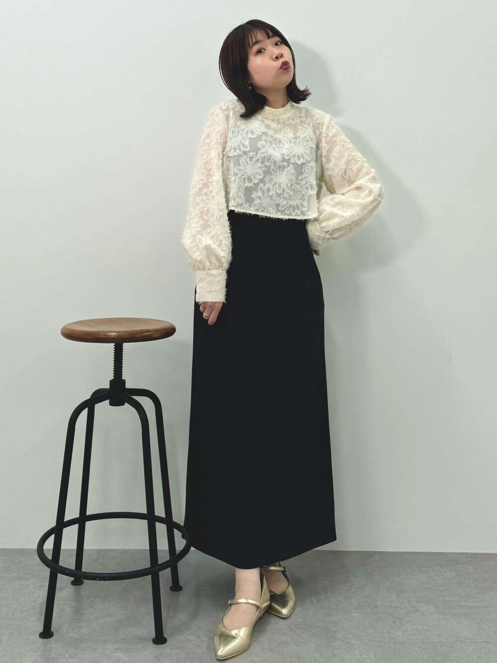 ベージュ系のドレス、ゴールド系のパンプス、ブラック系のバッグを着用したレディースの春コーディネートの2枚目の写真