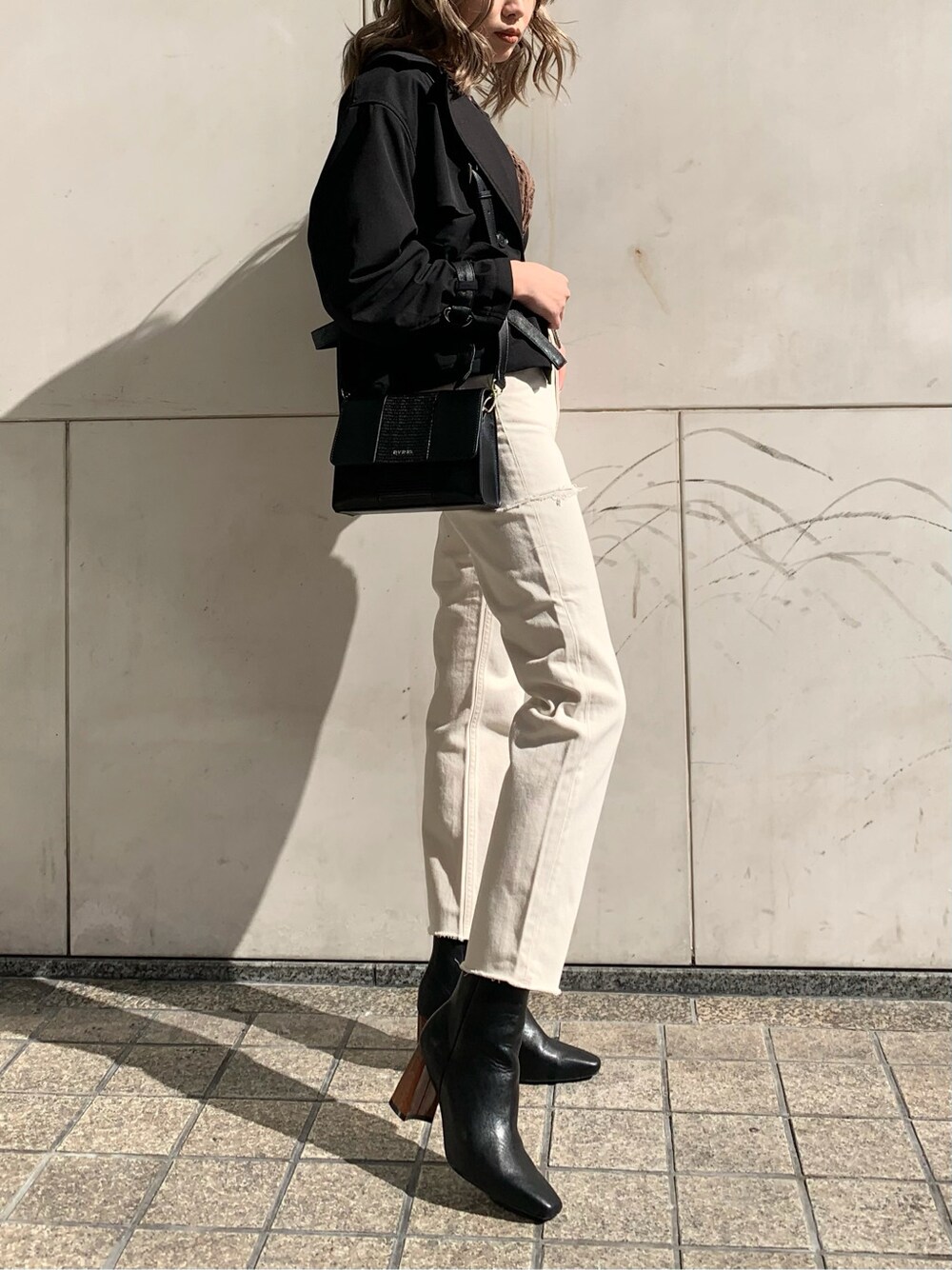 ブラック系のショルダーバッグ、ブラック系のトレンチコート、ホワイト系のデニムパンツを着用したレディースの冬コーディネートの2枚目の写真