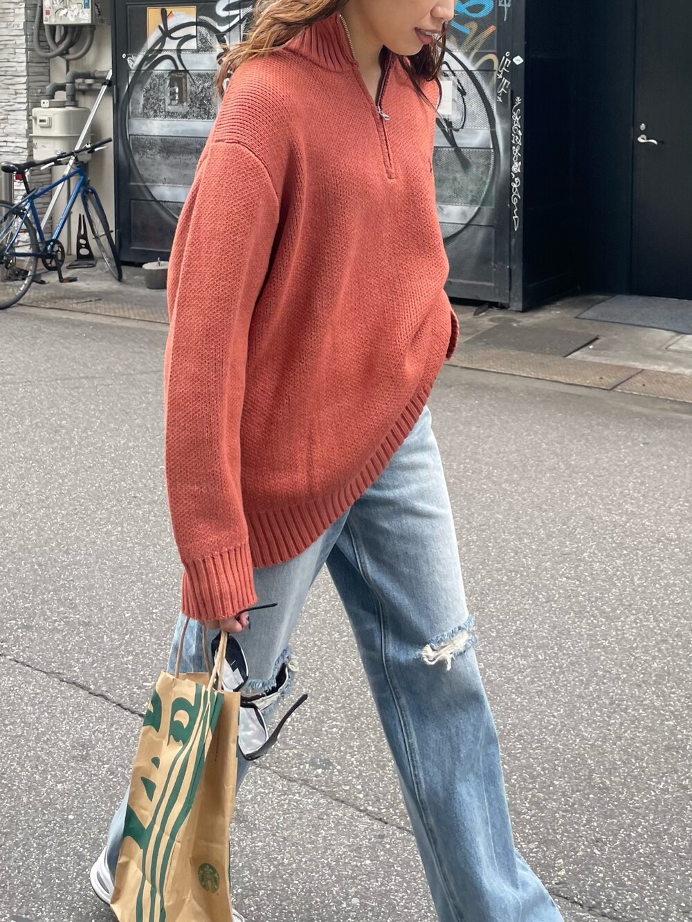 オレンジ系のニット/セーター、ブルー系のデニムパンツを着用したレディースの夏コーディネートの4枚目の写真