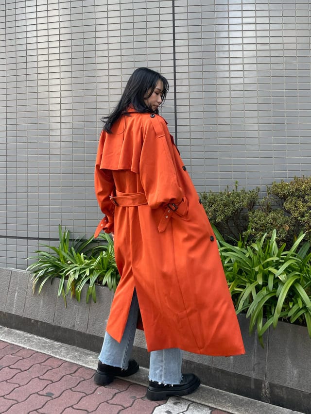 ブラック系のブーツ、オレンジ系のトレンチコート、ブルー系のデニムパンツを着用したレディースの春コーディネートの2枚目の写真