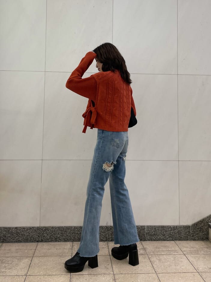 ブルー系のデニムパンツ、ブラック系のショルダーバッグ、オレンジ系のニット/セーターを着用したレディースの秋コーディネートの2枚目の写真