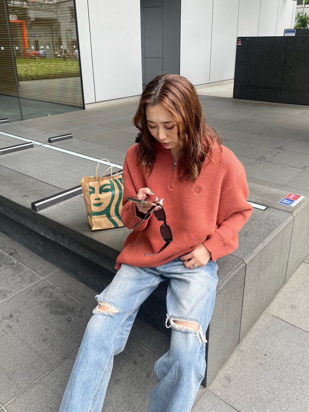 オレンジ系のニット/セーター、ブルー系のデニムパンツを着用したレディースの夏コーディネートの2枚目の写真