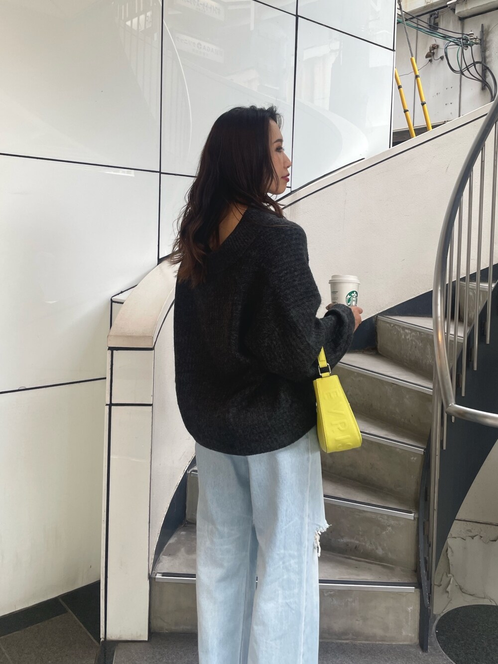 グレー系のニット/セーター、イエロー系のハンドバッグ、ブルー系のデニムパンツを着用したレディースの秋コーディネートの5枚目の写真