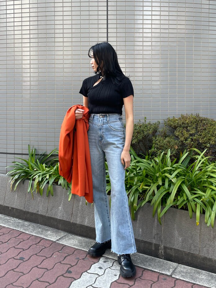 ブラック系のニット/セーター、オレンジ系のトレンチコート、ブルー系のデニムパンツを着用したレディースの春コーディネートの5枚目の写真