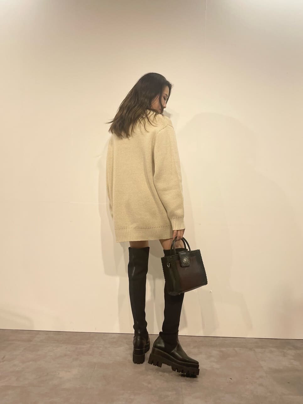 ブラック系のショルダーバッグ、ホワイト系のニット/セーター、ブラック系のブーツを着用したレディースの秋コーディネートの2枚目の写真