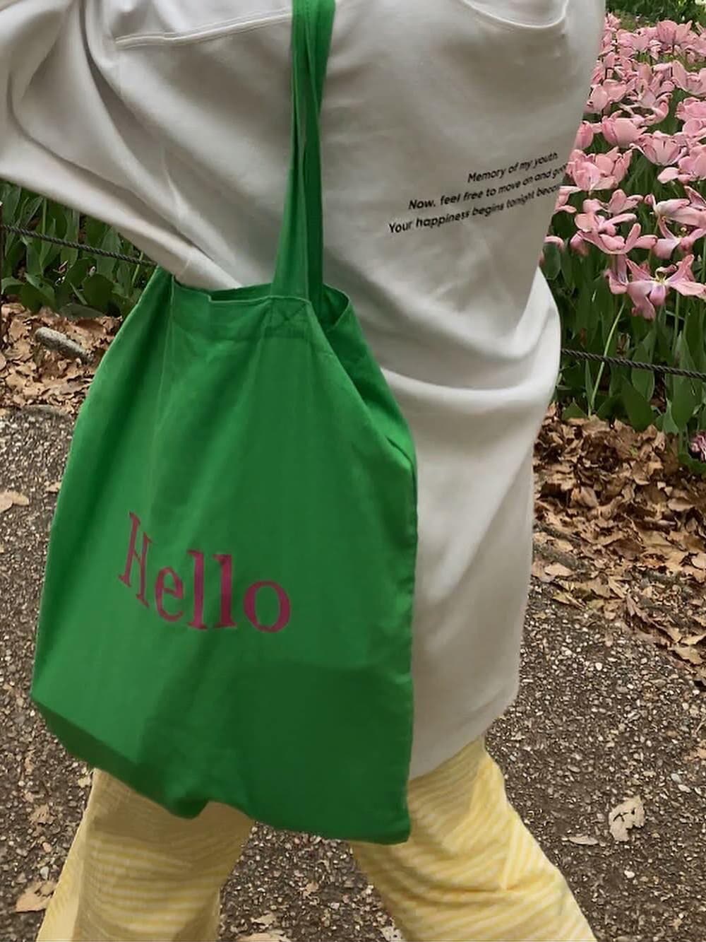 ホワイト系のトップス、グリーン系のトートバッグ、イエロー系のパンツを着用したレディースの夏コーディネートの2枚目の写真