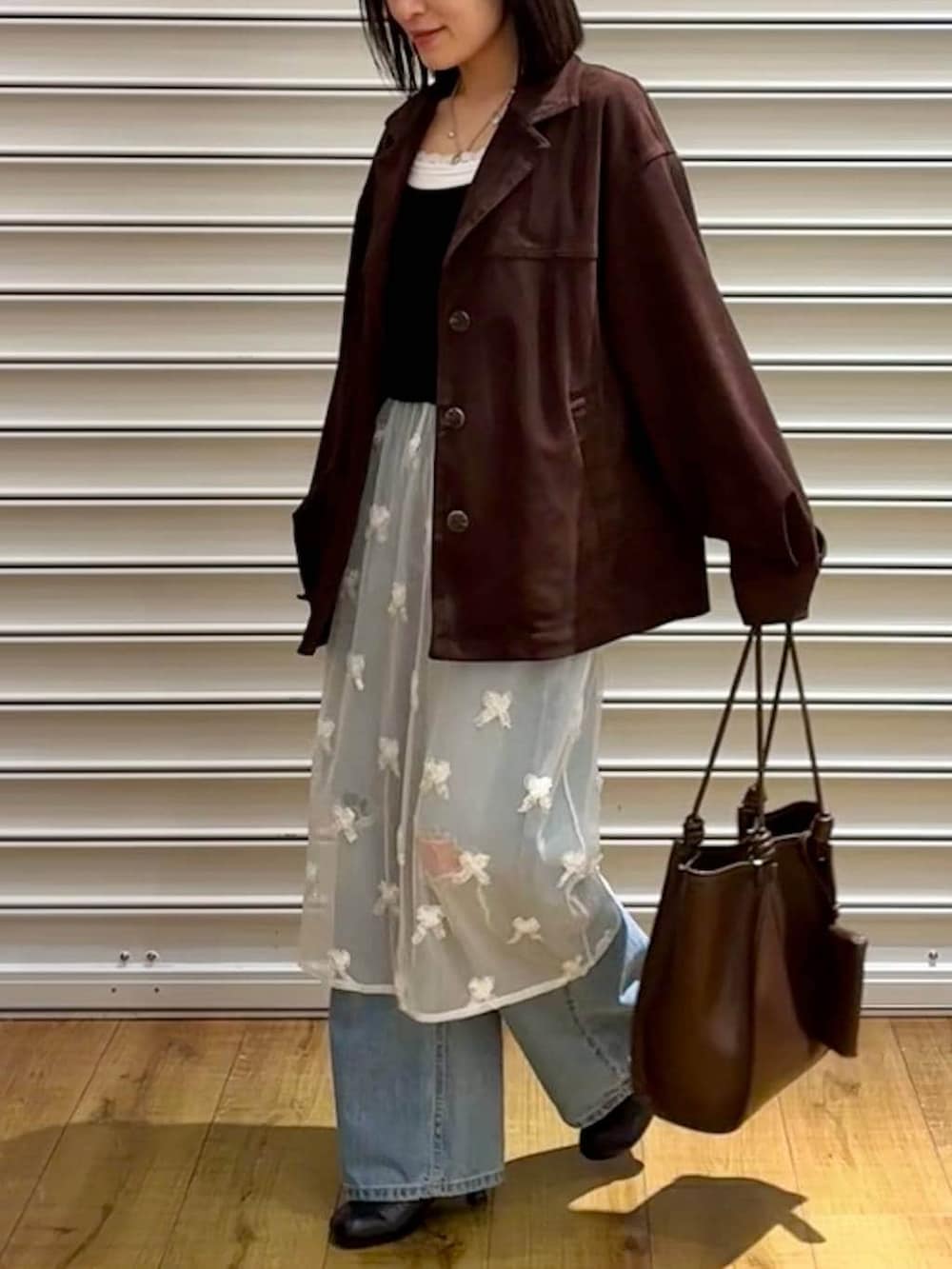 ブルー系のデニムパンツ、ブラウン系のテーラードジャケット、ブラック系のサンダルを着用したレディースの春コーディネートの3枚目の写真