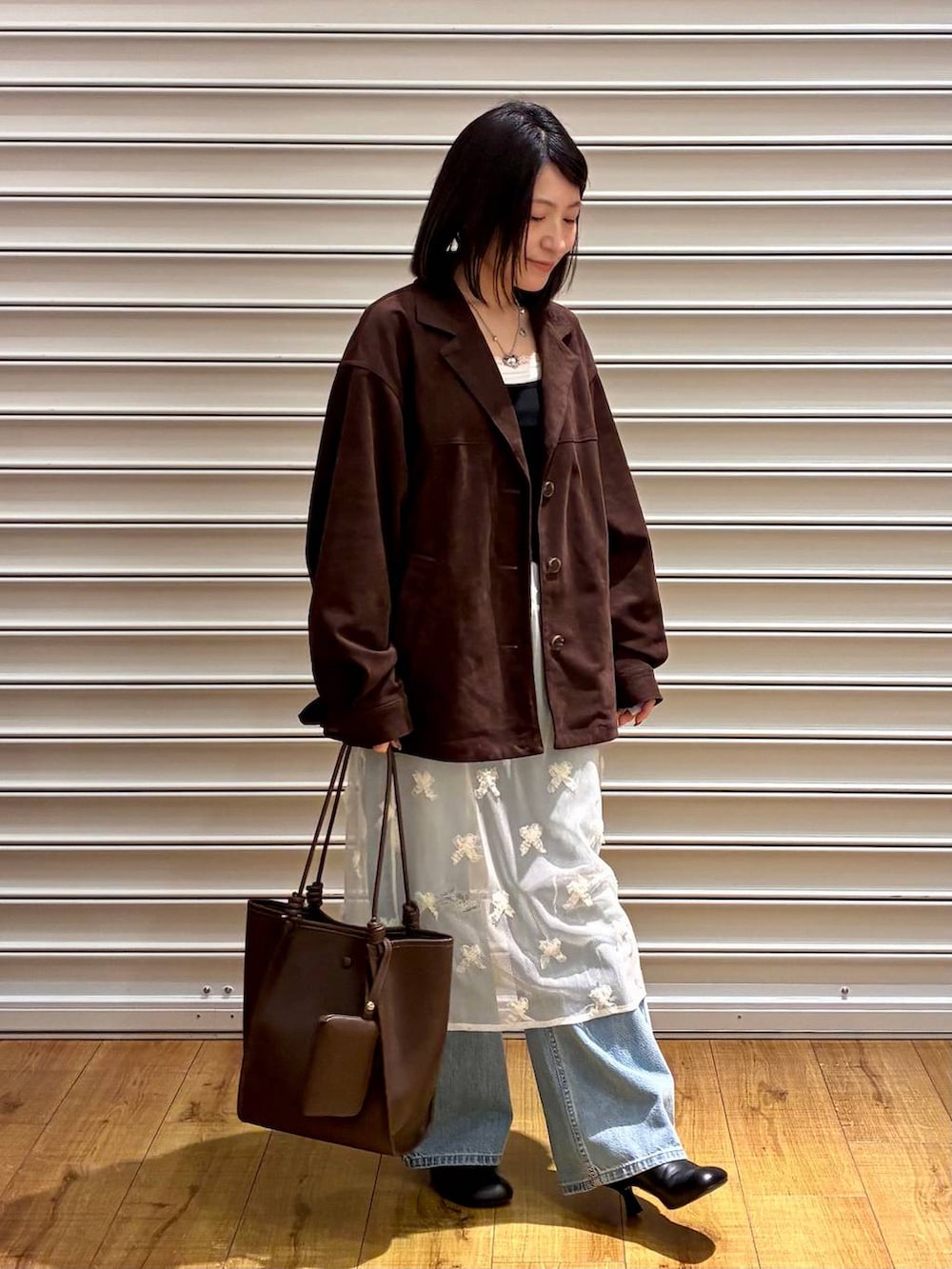 ブルー系のデニムパンツ、ブラウン系のテーラードジャケット、ブラック系のサンダルを着用したレディースの春コーディネートの2枚目の写真