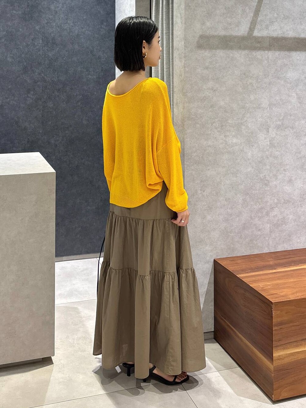 ブラック系のショルダーバッグ、ブラック系のサンダル、イエロー系のニット/セーターを着用したレディースの夏コーディネートの2枚目の写真