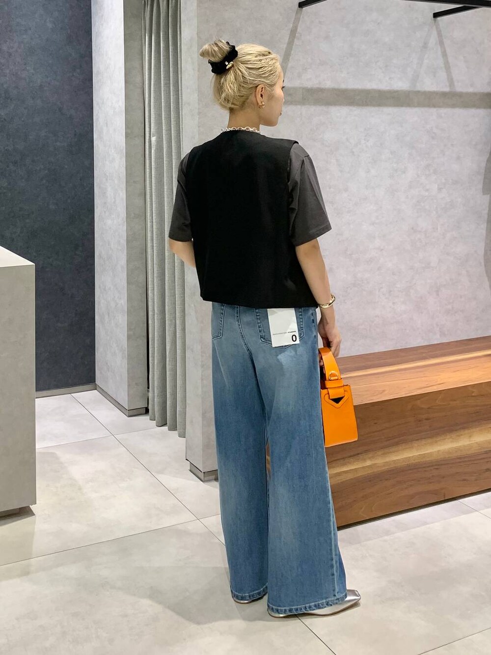 オレンジ系のハンドバッグ、ブルー系のデニムパンツ、シルバー系のパンプスを着用したレディースの夏コーディネートの2枚目の写真