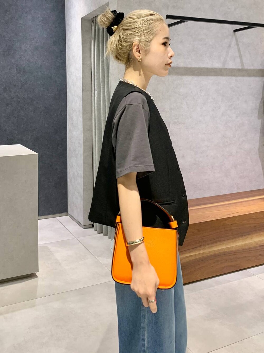 オレンジ系のハンドバッグ、ブルー系のデニムパンツ、シルバー系のパンプスを着用したレディースの夏コーディネートの4枚目の写真