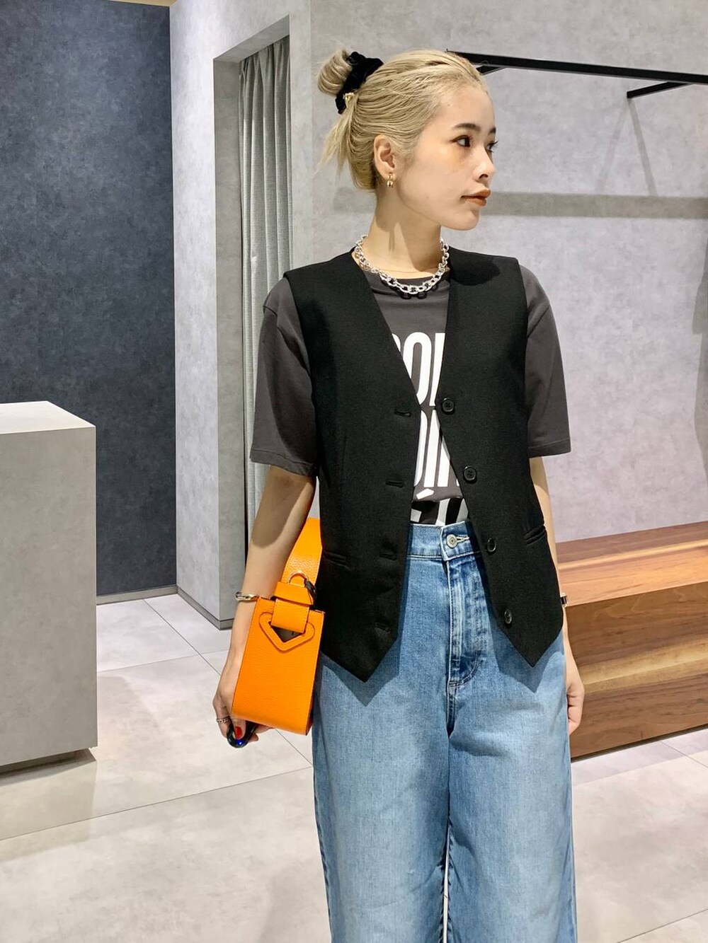 オレンジ系のハンドバッグ、ブルー系のデニムパンツ、シルバー系のパンプスを着用したレディースの夏コーディネートの3枚目の写真