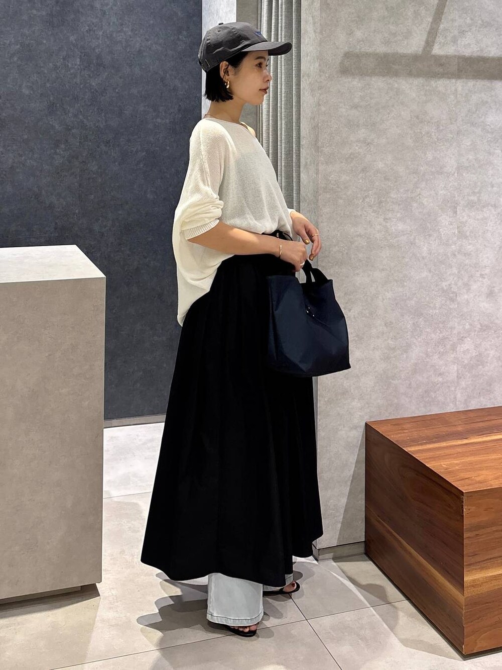 ブルー系のデニムパンツ、ブルー系のトートバッグ、ホワイト系のニット/セーターを着用したレディースの夏コーディネートの2枚目の写真