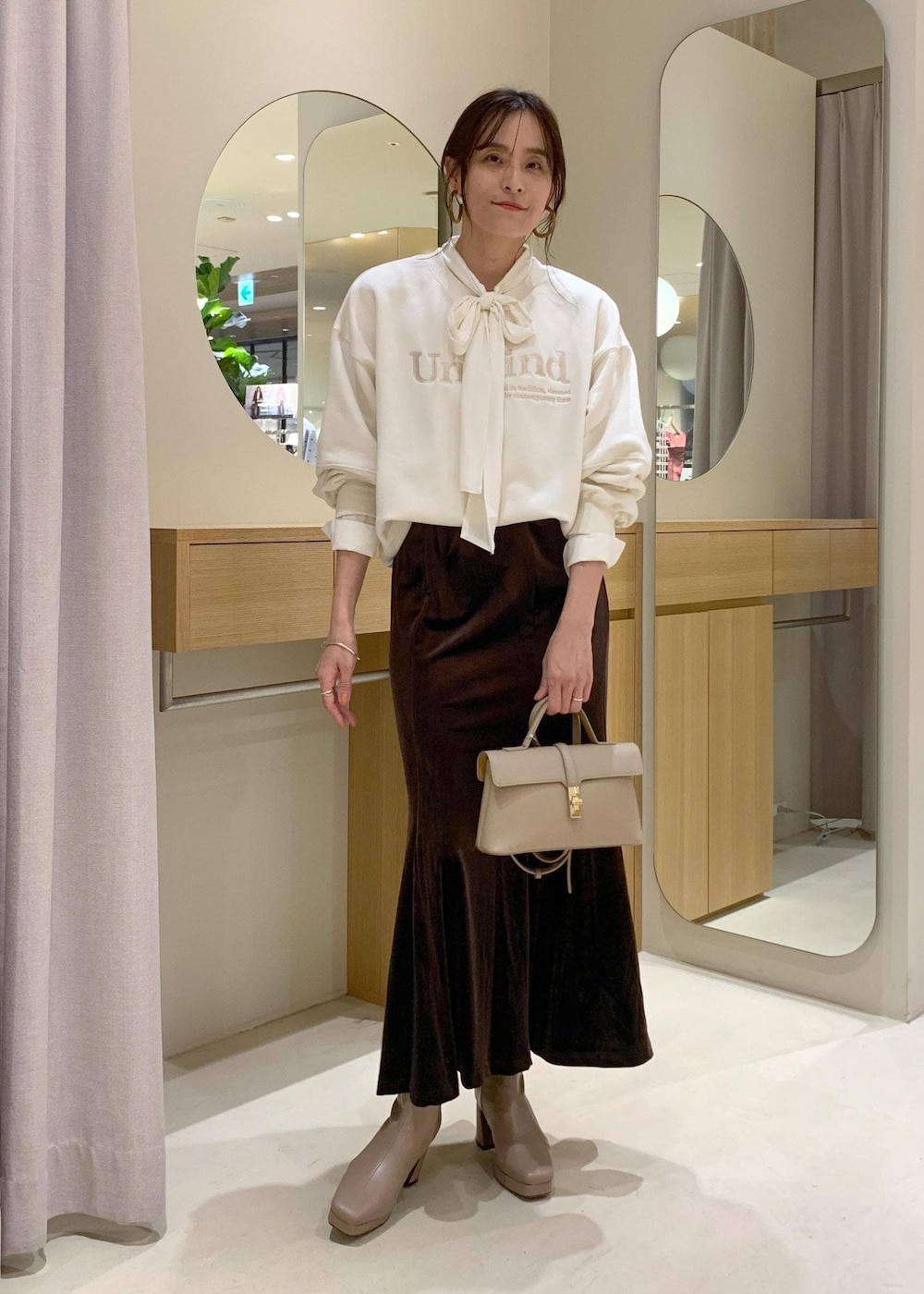 ベージュ系のショルダーバッグ、ブラウン系のスカート、ベージュ系のブーツを着用したレディースの秋コーディネートの2枚目の写真