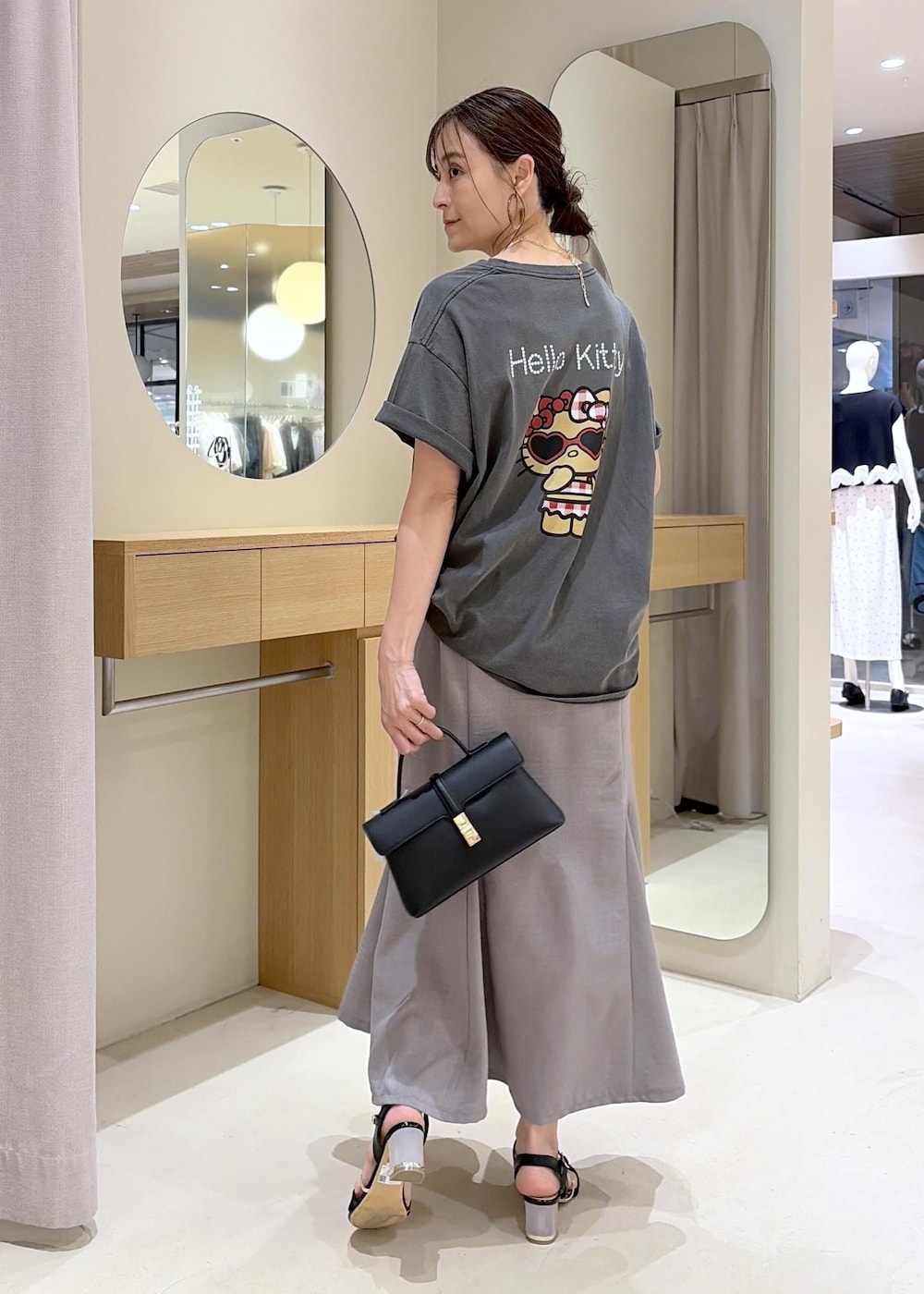 ブラック系のショルダーバッグ、グレー系のスカート、ブラック系のサンダルを着用したレディースの夏コーディネートの2枚目の写真