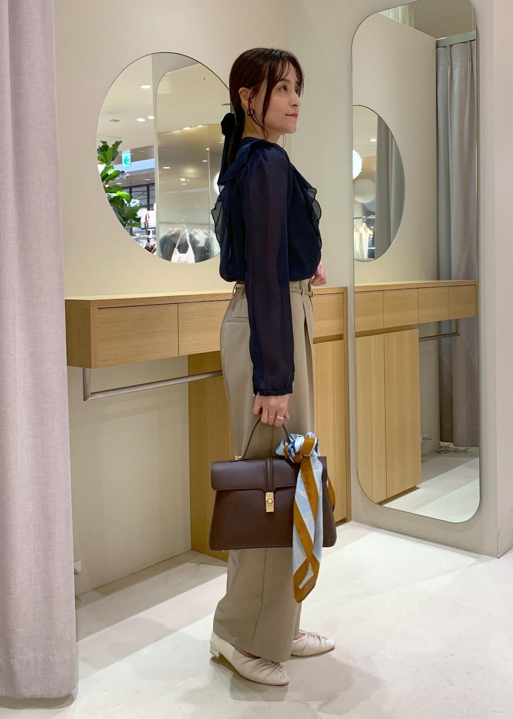 ブラウン系のハンドバッグ、ホワイト系のパンプス、ブルー系のシャツ/ブラウスを着用したレディースの秋コーディネートの3枚目の写真