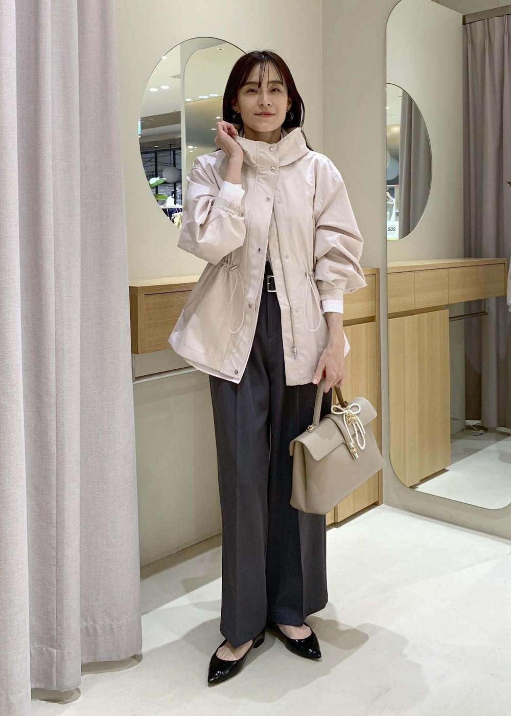 ベージュ系のハンドバッグ、ピンク系のナイロンジャケット、グレー系のスラックスを着用したレディースの春コーディネートの2枚目の写真