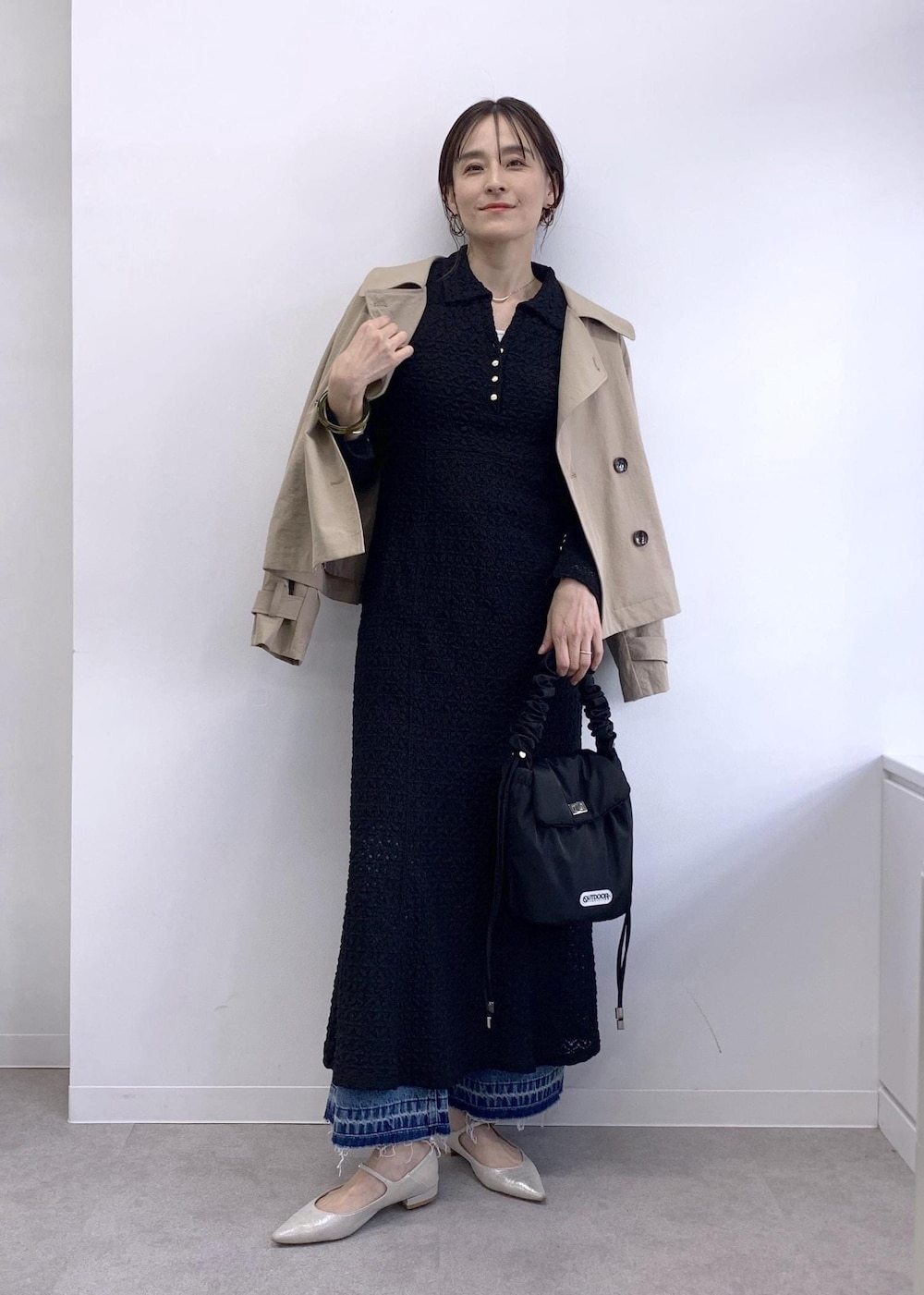 ブラック系のショルダーバッグ、ベージュ系のトレンチコート、ブルー系のデニムパンツを着用したレディースの冬コーディネートの2枚目の写真