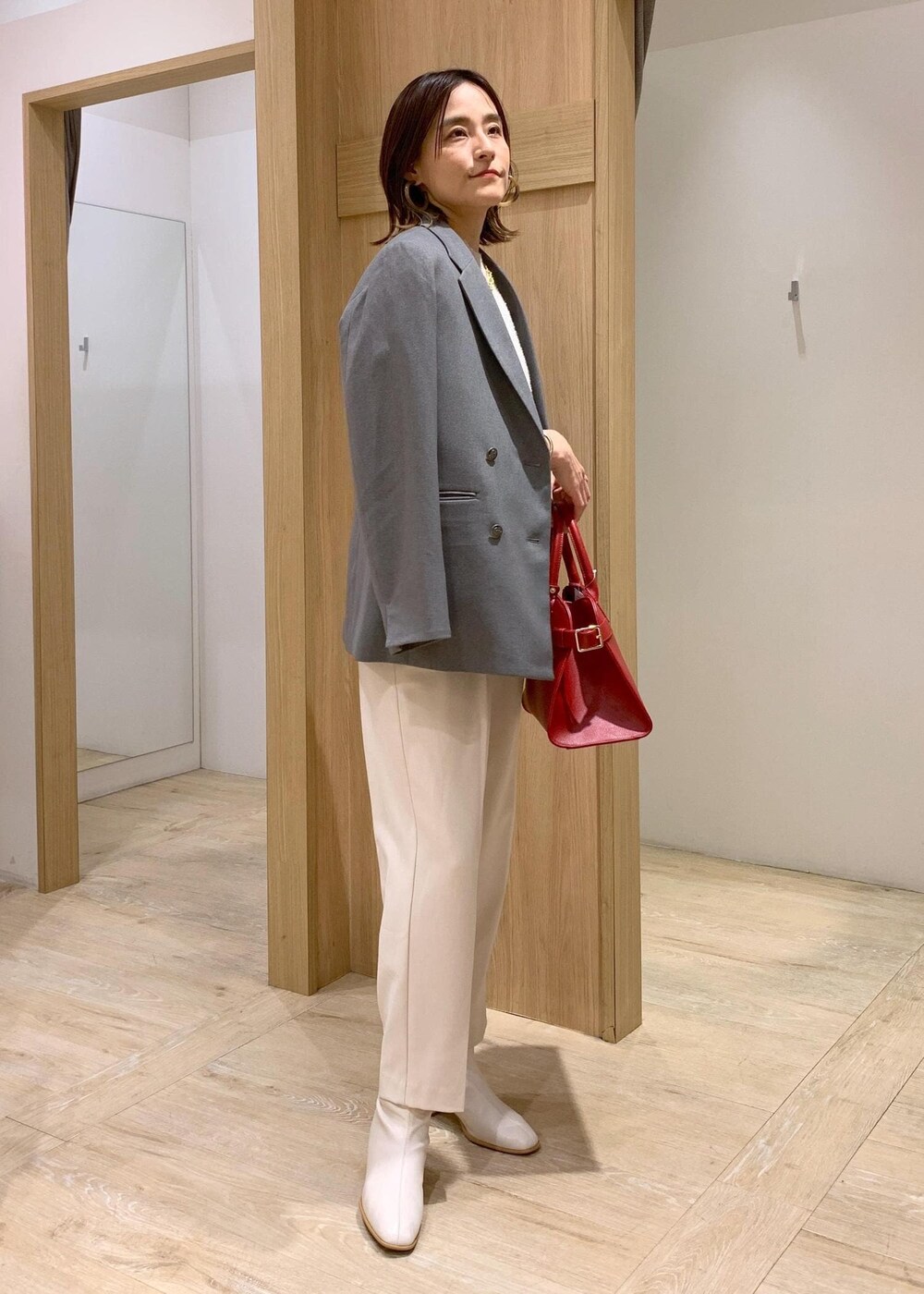 レッド系のトートバッグ、ホワイト系のブーツ、グレー系のテーラードジャケットを着用したレディースの冬コーディネートの2枚目の写真