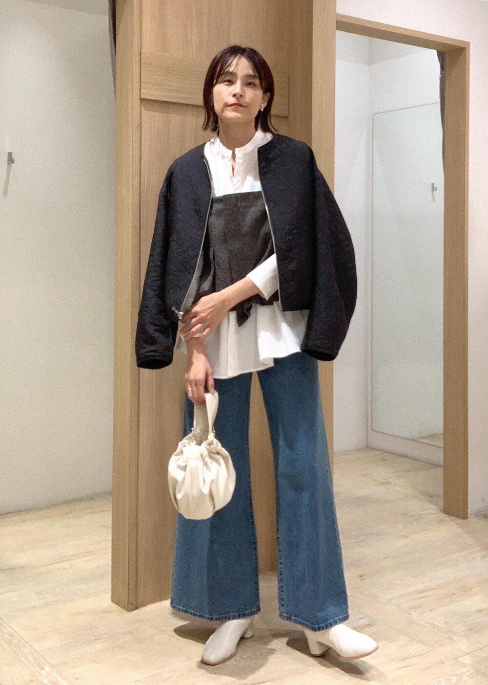 ホワイト系のハンドバッグ、ブルー系のデニムパンツ、ホワイト系のブーツを着用したレディースの秋コーディネートの2枚目の写真