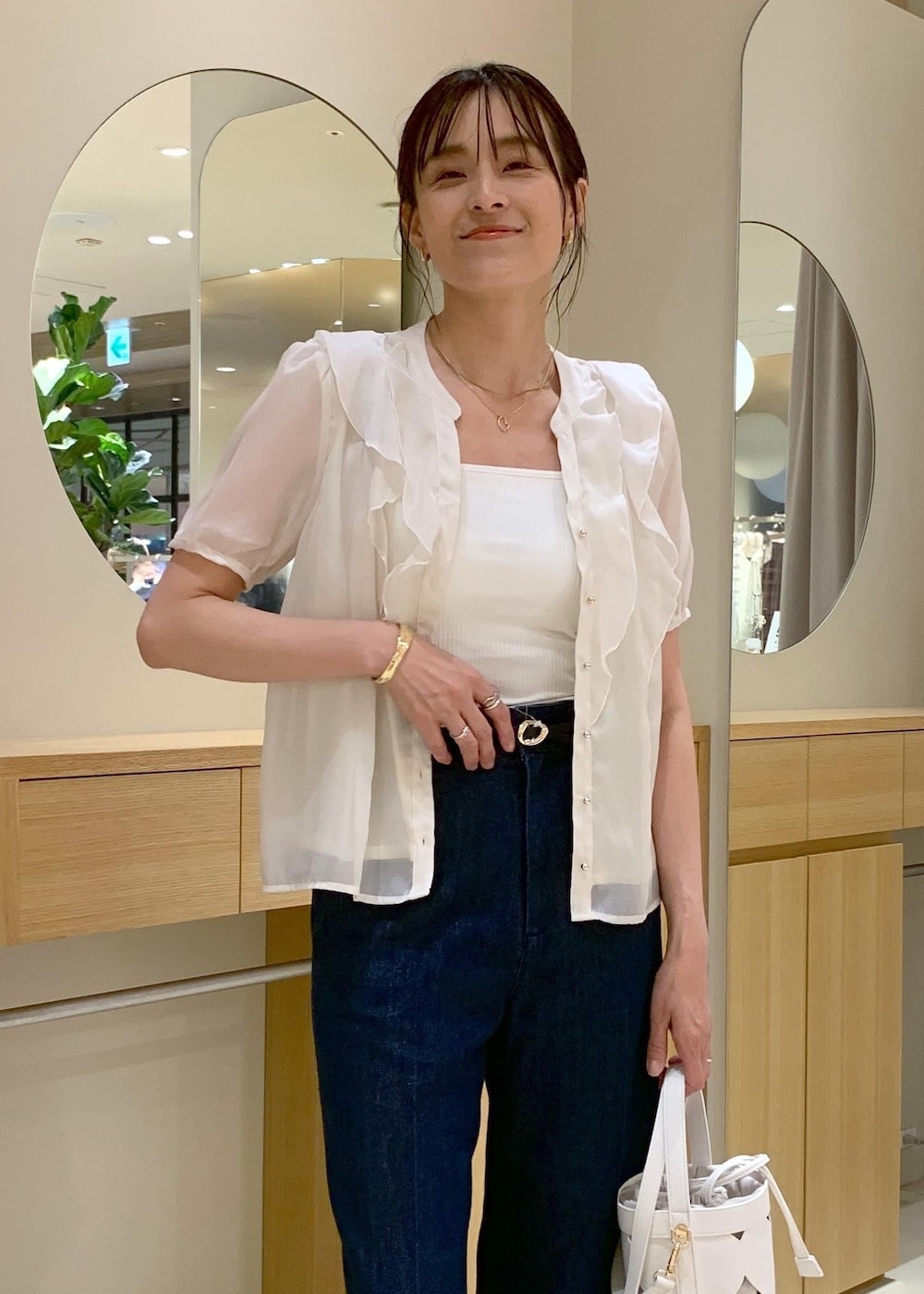 ホワイト系のキャミソール、ブラック系のサンダル、ブルー系のデニムパンツを着用したレディースの夏コーディネートの4枚目の写真