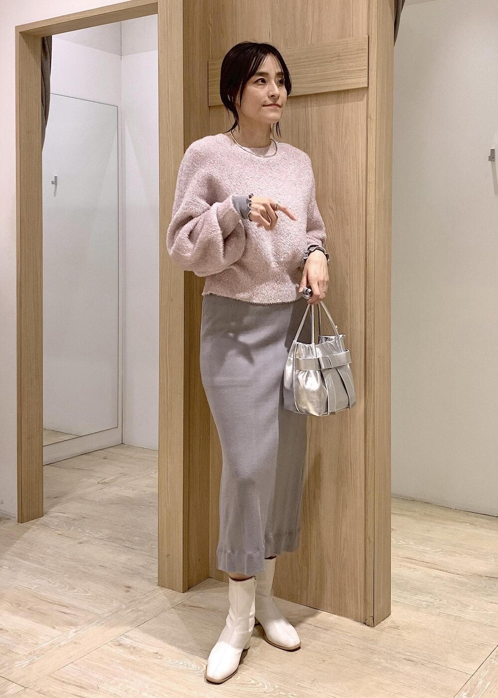 シルバー系のショルダーバッグ、ホワイト系のブーツ、グレー系のワンピースを着用したレディースの冬コーディネートの2枚目の写真