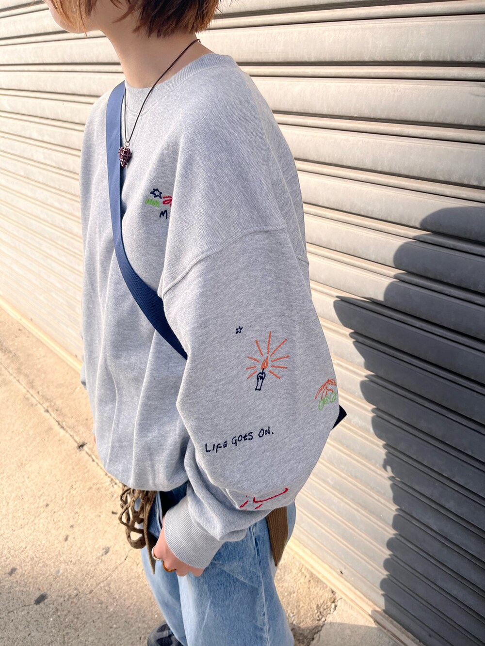 ブルー系のデニムパンツ、ブルー系のショルダーバッグ、グレー系のスウェットを着用したレディースの秋コーディネートの3枚目の写真