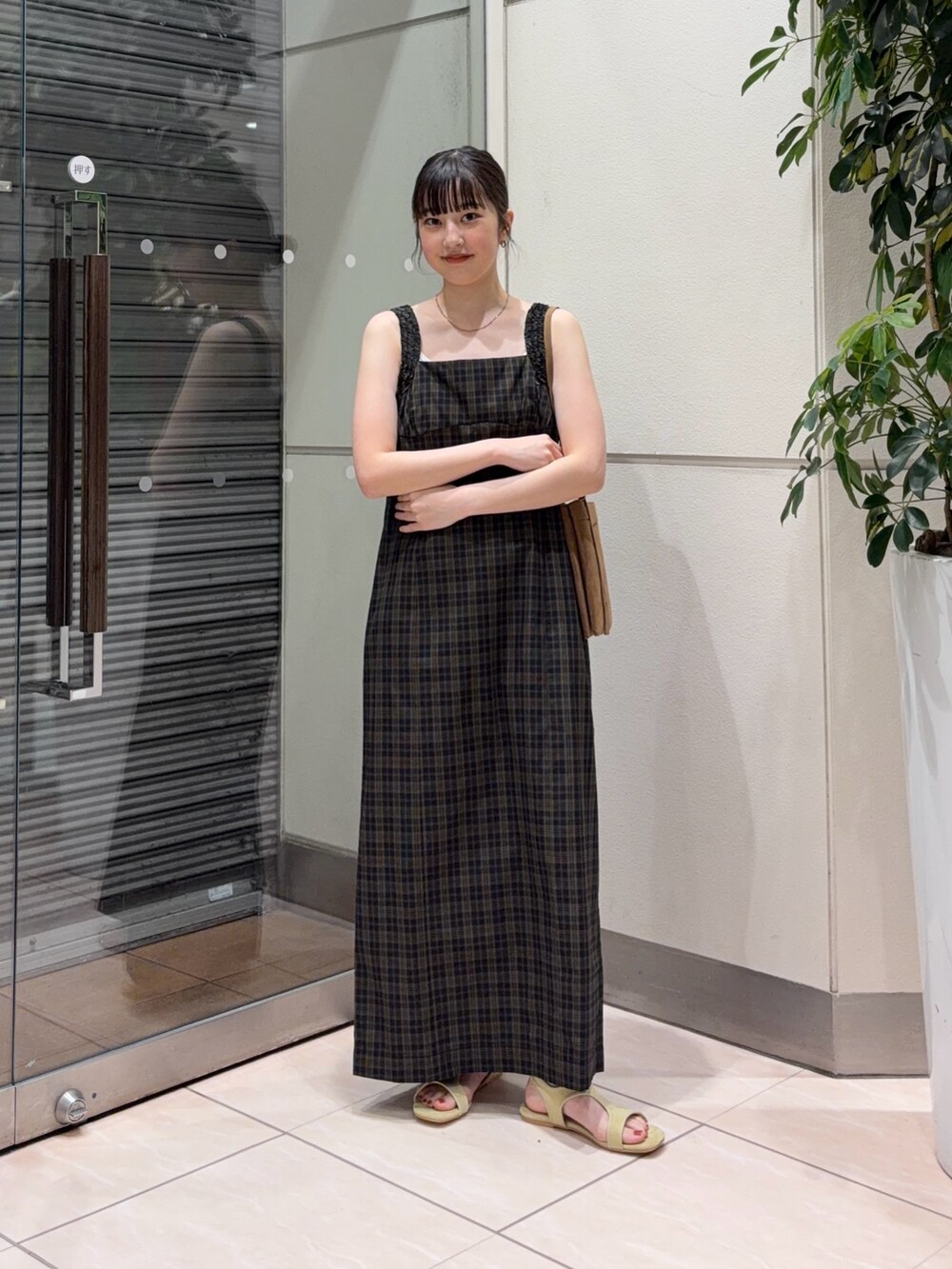 イエロー系のサンダル、イエロー系のショルダーバッグ、ブラック系のワンピースを着用したレディースの夏コーディネートの2枚目の写真