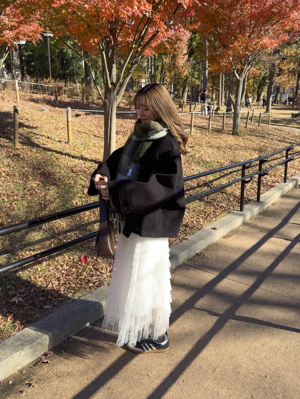 ブラック系のステンカラーコート、ブラウン系のショルダーバッグ、ホワイト系のスカートを着用したレディースの冬コーディネートの3枚目の写真