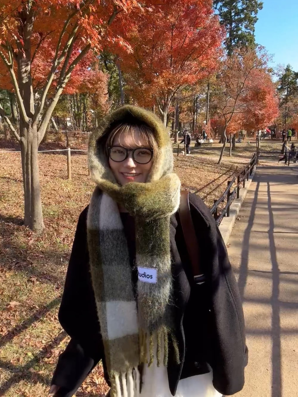 ブラック系のステンカラーコート、ブラウン系のショルダーバッグ、ホワイト系のスカートを着用したレディースの冬コーディネートの4枚目の写真