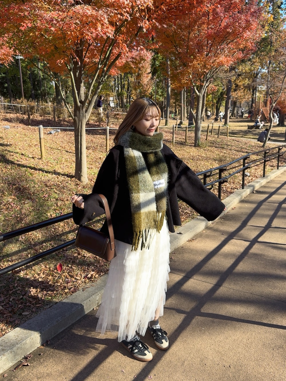 ブラック系のステンカラーコート、ブラウン系のショルダーバッグ、ホワイト系のスカートを着用したレディースの冬コーディネートの2枚目の写真