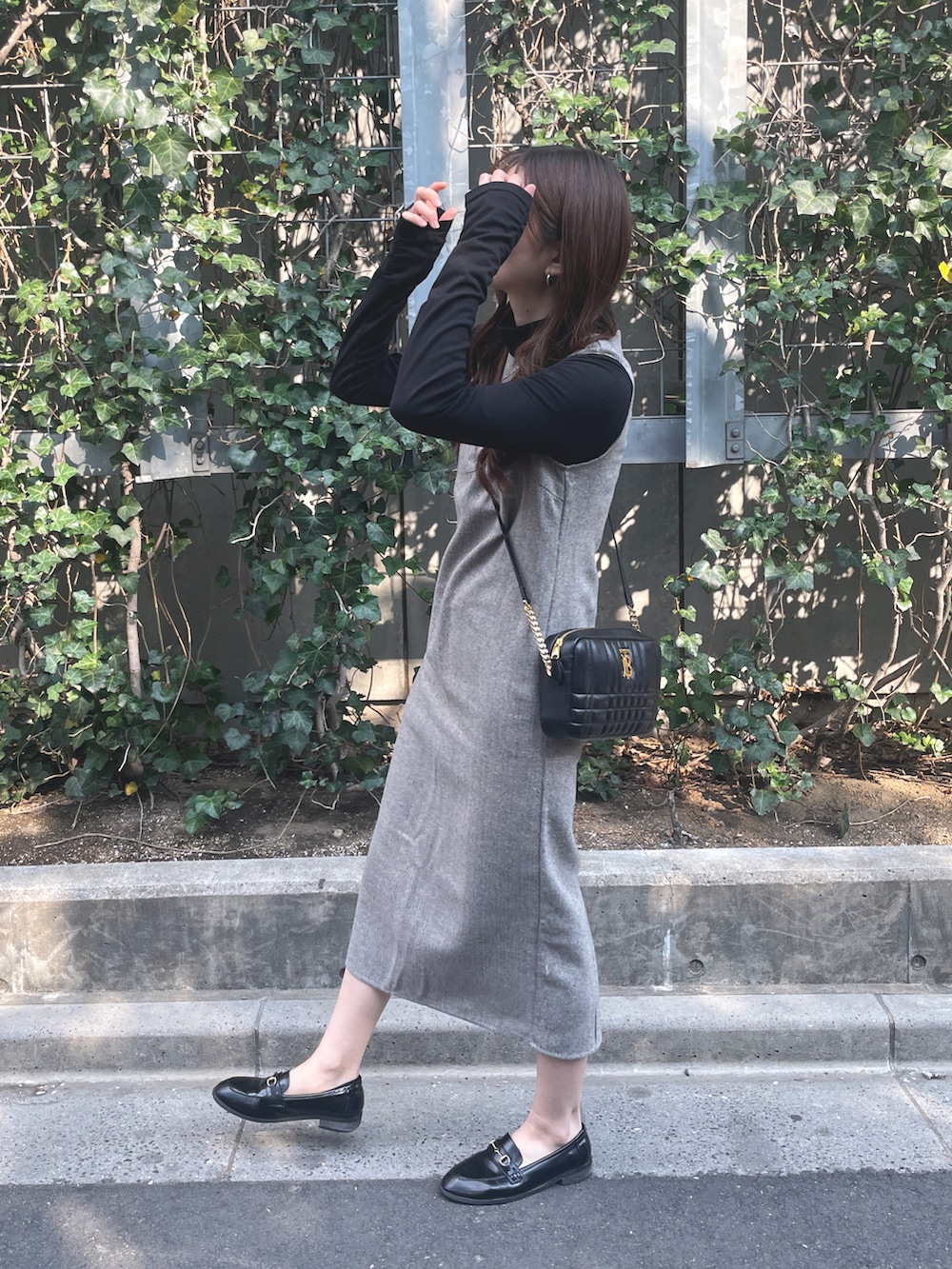 グレー系のジャンパースカート、ブラック系のショルダーバッグ、ブラック系のローファーを着用したレディースの春コーディネートの2枚目の写真