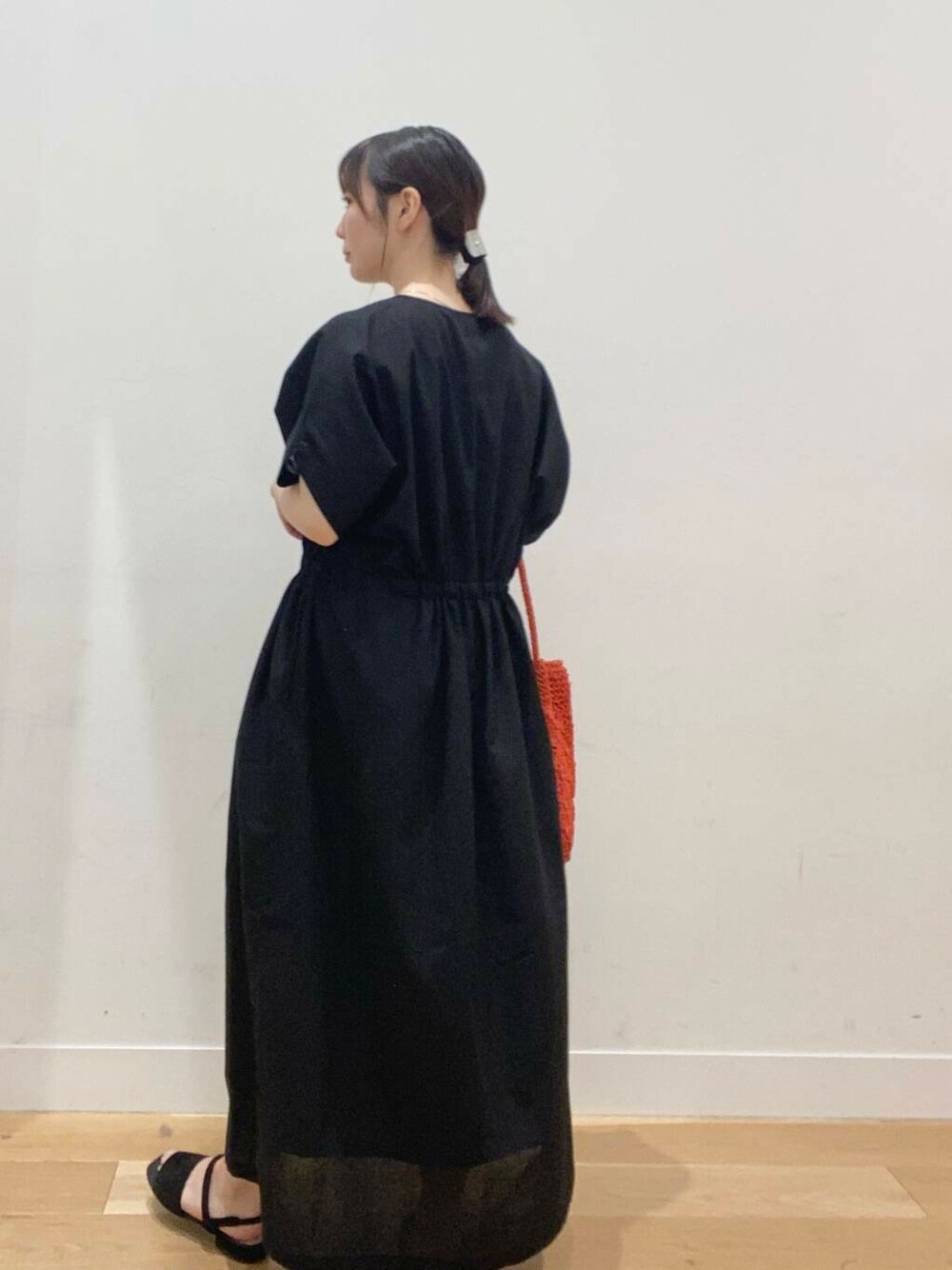 オレンジ系のトートバッグ、ブラック系のワンピース、ブラック系のサンダルを着用したレディースの夏コーディネートの3枚目の写真