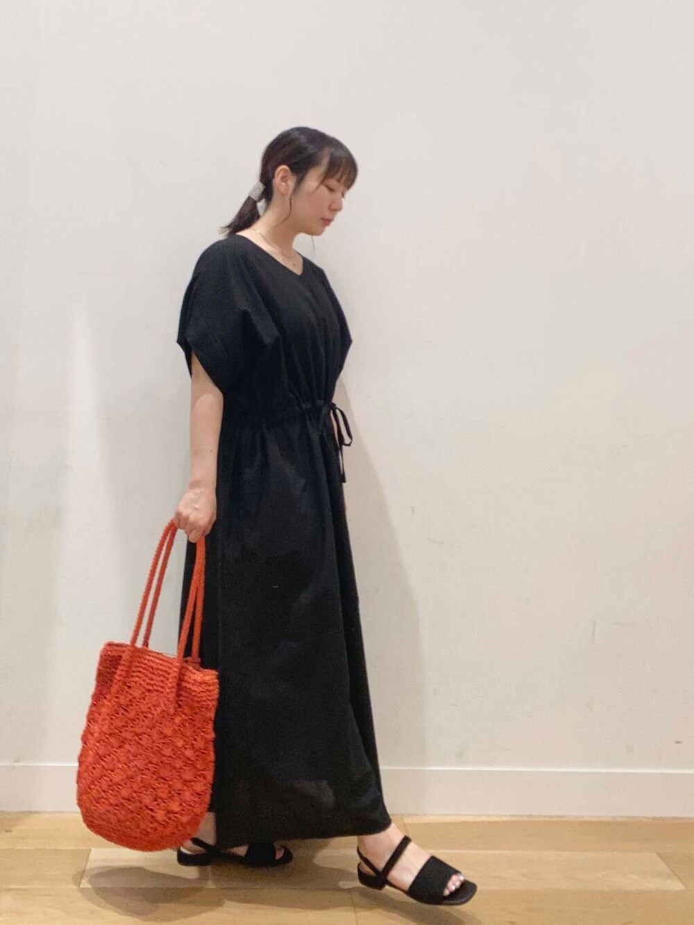オレンジ系のトートバッグ、ブラック系のワンピース、ブラック系のサンダルを着用したレディースの夏コーディネートの2枚目の写真