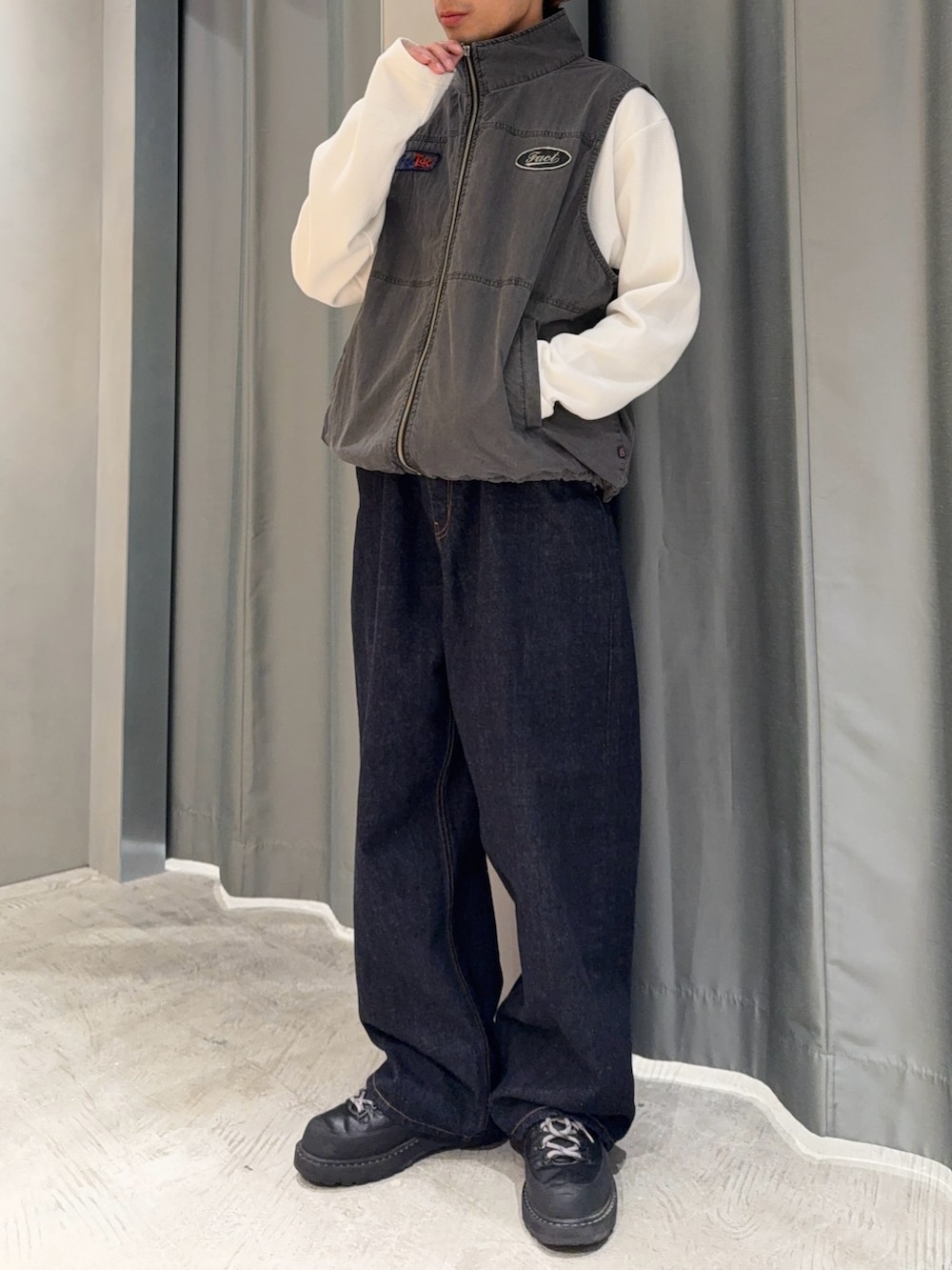 ブルー系のデニムパンツ、ブラック系のブーツ、グレー系のベストを着用したメンズの春コーディネートの2枚目の写真