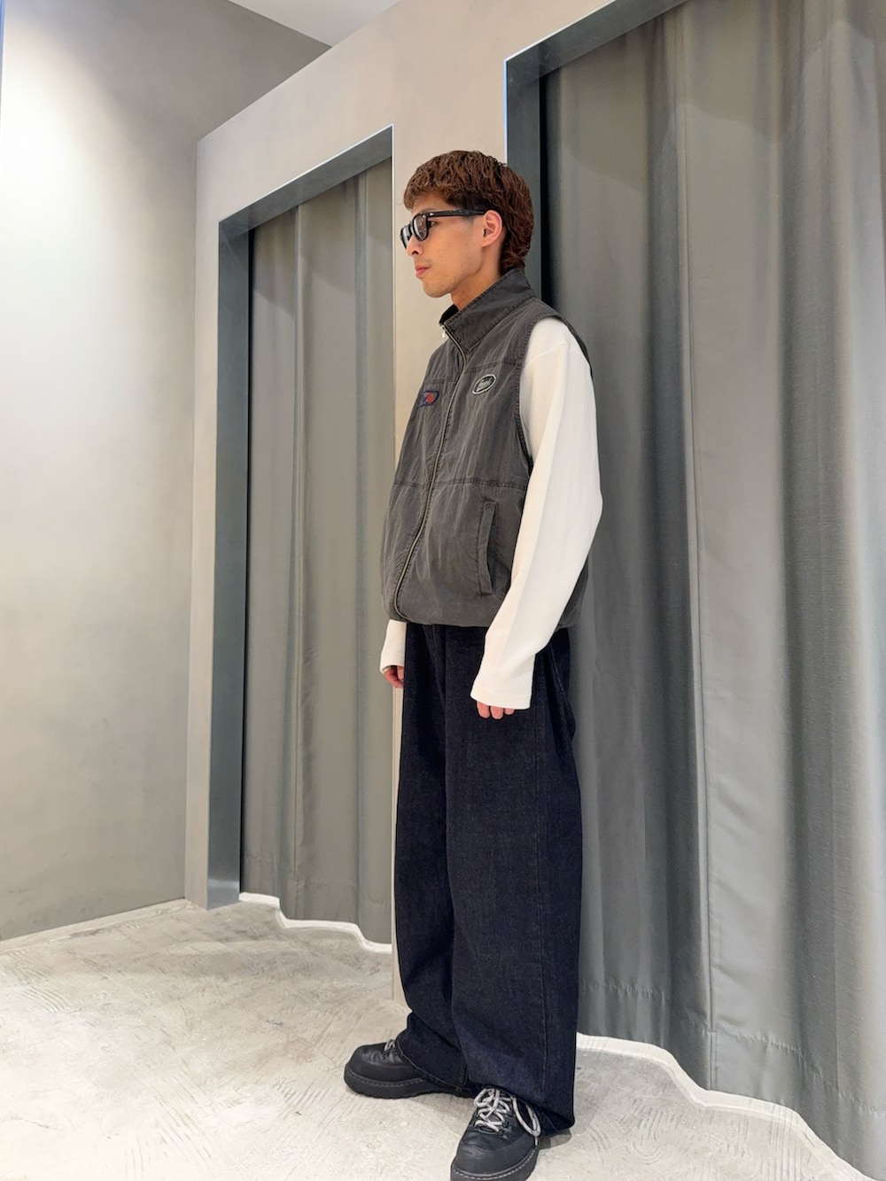 ブルー系のデニムパンツ、ブラック系のブーツ、グレー系のベストを着用したメンズの春コーディネートの3枚目の写真