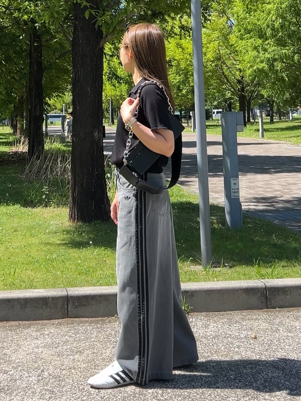 グレー系のデニムパンツ、ブラック系のポロシャツ、ホワイト系のスニーカーを着用したレディースの夏コーディネートの2枚目の写真