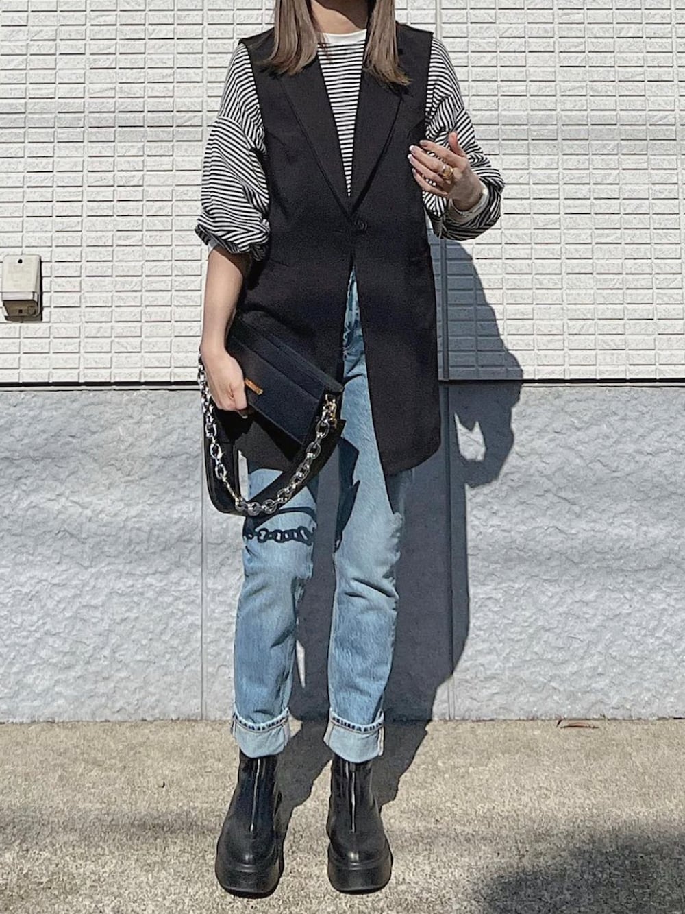 ブラック系のベスト、ブラック系のバッグ、ブラック系のブーツを着用したレディースの春コーディネートの2枚目の写真