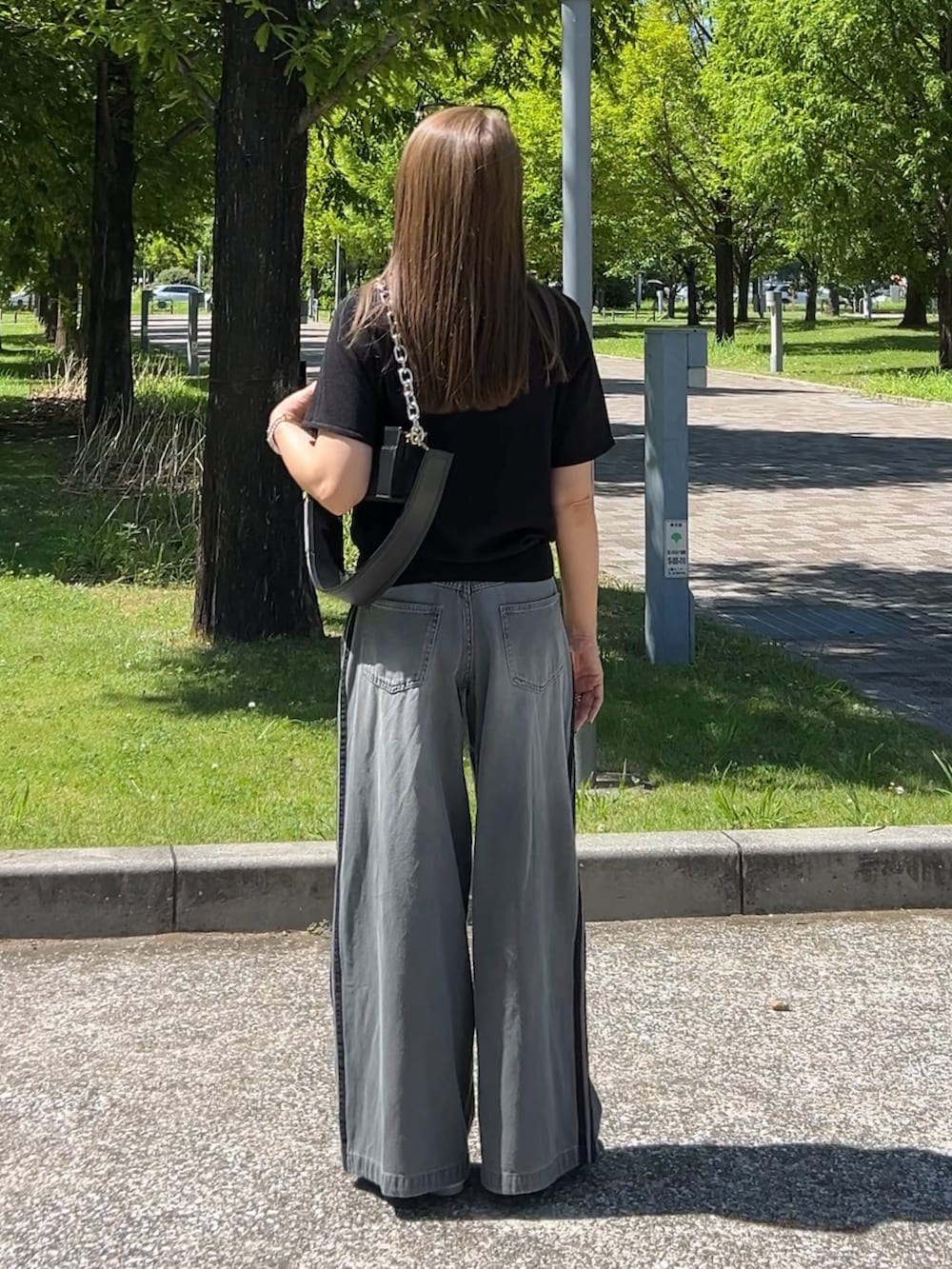 グレー系のデニムパンツ、ブラック系のポロシャツ、ホワイト系のスニーカーを着用したレディースの夏コーディネートの3枚目の写真