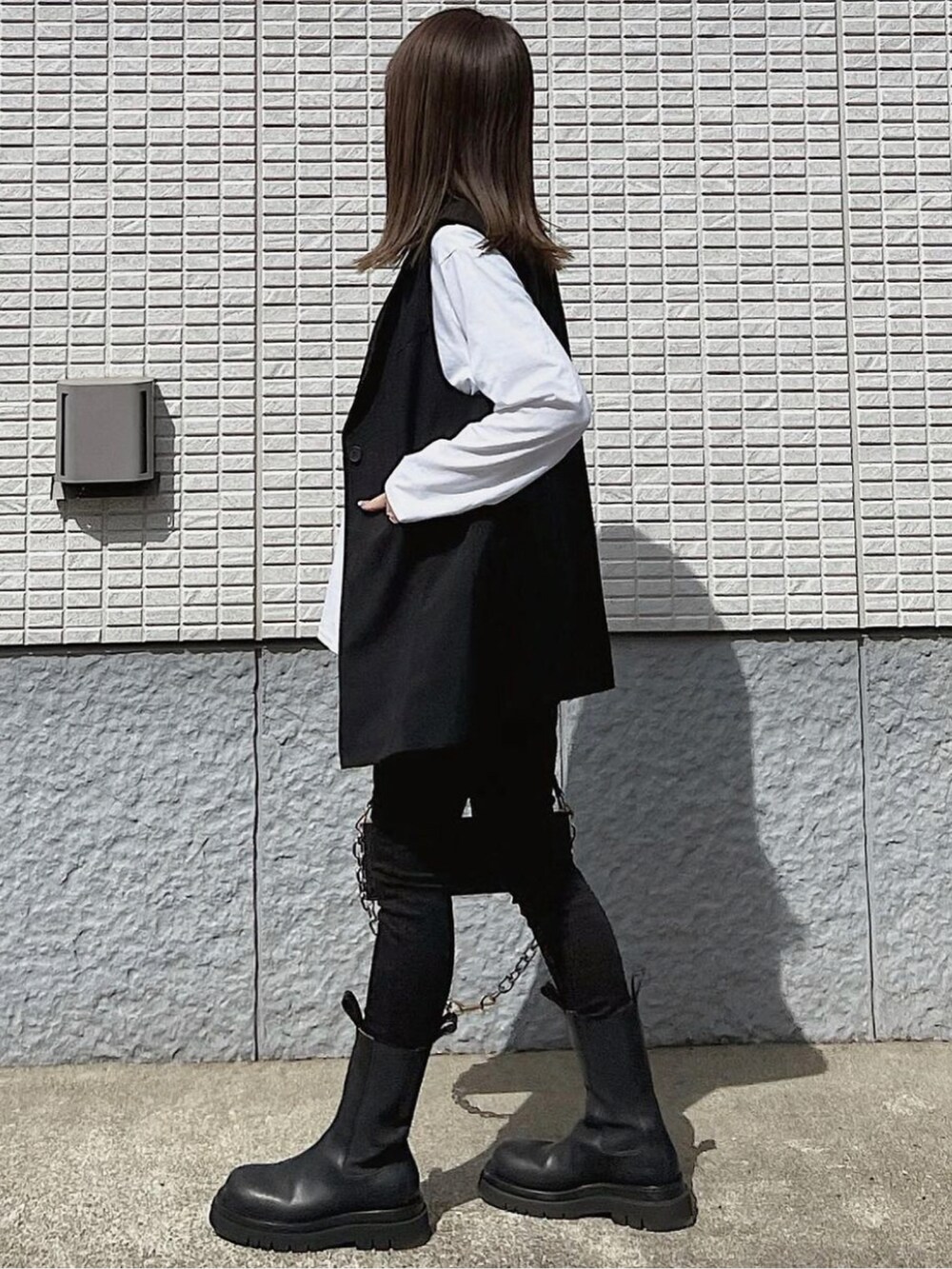 ブラック系のベスト、ブラック系のバッグ、ブラック系のブーツを着用したレディースの春コーディネートの4枚目の写真