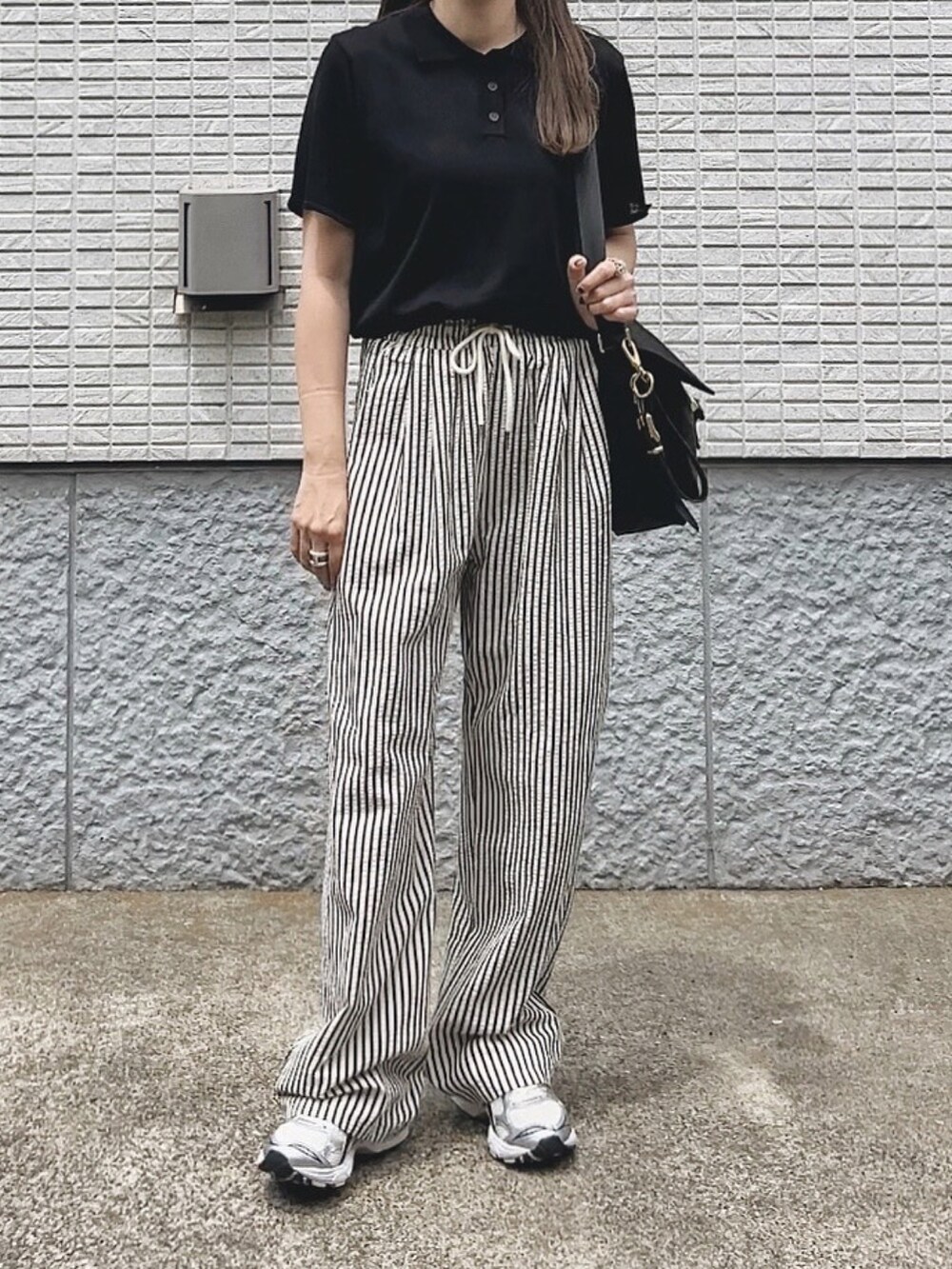 ブラック系のバッグ、ブラック系のポロシャツ、ホワイト系のスニーカーを着用したレディースの春コーディネートの2枚目の写真