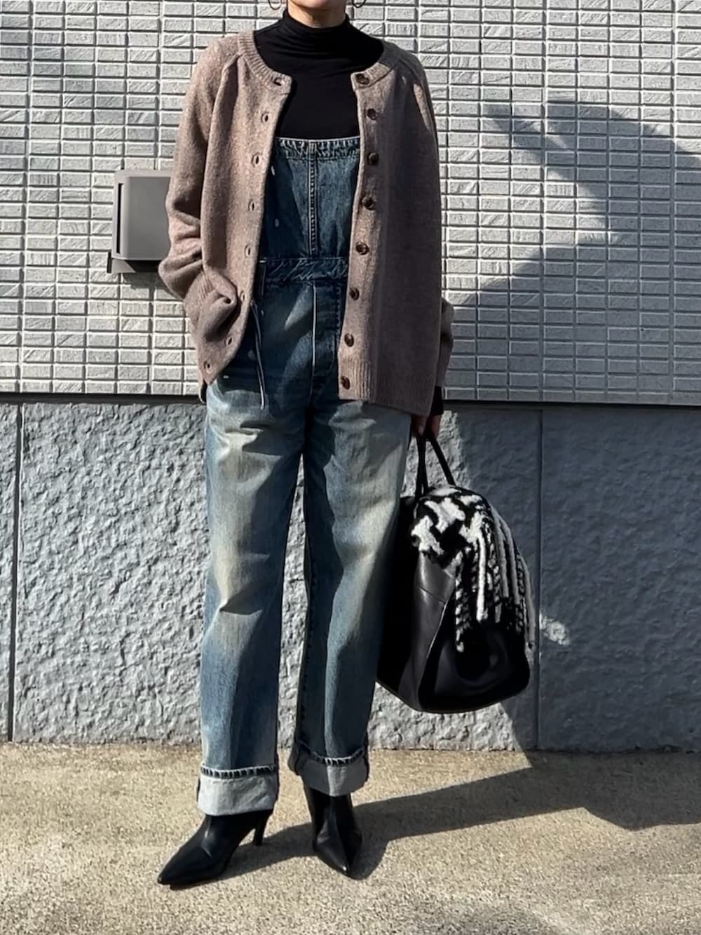 ベージュ系のカーディガン/ボレロ、ブルー系のサロペット/オーバーオール、ブラック系のブーツを着用したレディースの冬コーディネートの3枚目の写真